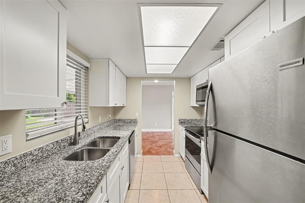 A galley kitchen features white cabinets, granite countertops, stainless steel appliances, and tile flooring — 7925 SEGOVIA STREET, ORLANDO, FL