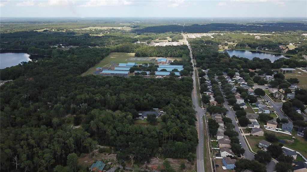 An aerial view shows a residential neighborhood, a school complex, and surrounding wooded areas — E BATES AVENUE, EUSTIS, FL