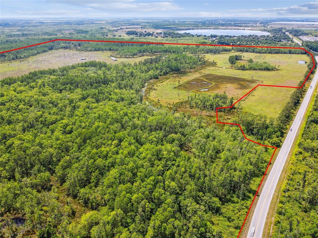 An aerial view shows a large, partially wooded plot of land bordered by a road — 0 ST RD 557, LAKE ALFRED, FL