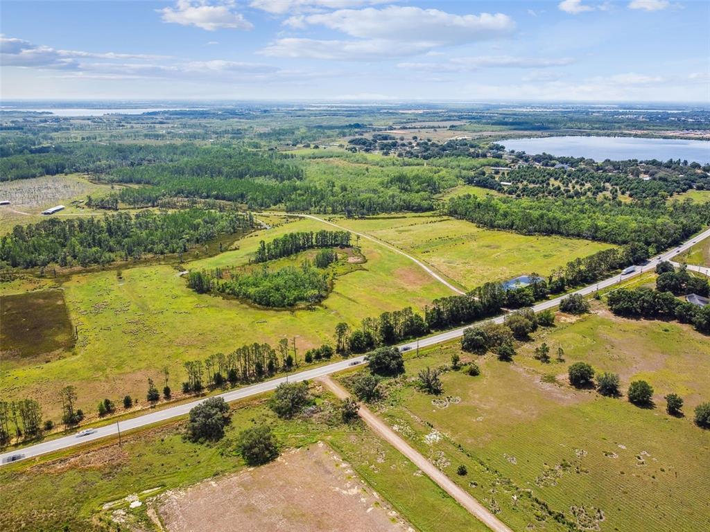 An aerial view shows a rural landscape with a paved road, open fields, and trees — 0 ST RD 557, LAKE ALFRED, FL