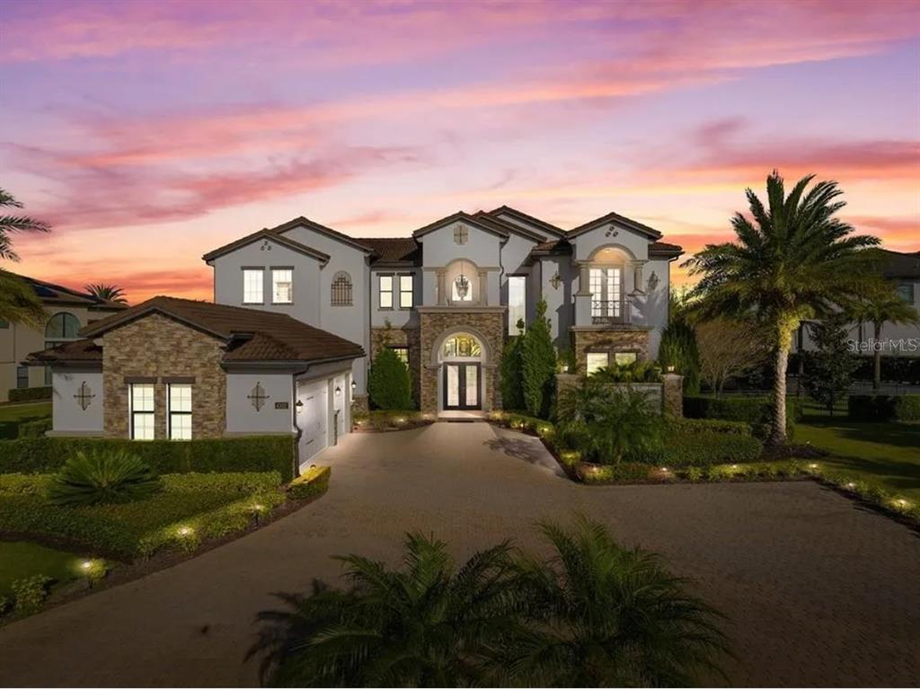 A large two-story house with a stone facade, arched entryway, and a paved driveway at sunset — 4302 ISABELLA CIR, WINDERMERE, FL