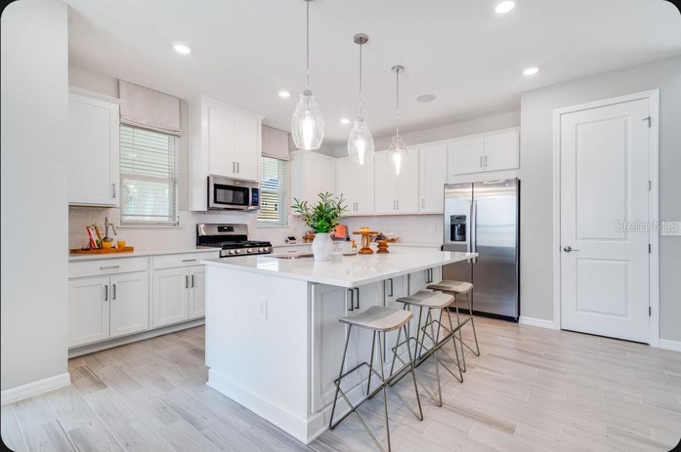 A bright kitchen features white cabinets, a large quartz island, stainless appliances, and light flooring — 5162 DOMINION ALLEY, ST CLOUD, FL