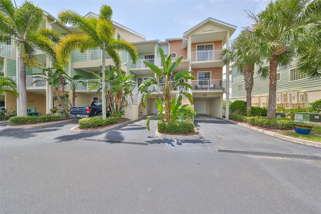 A multi-story residential building with pastel siding, balconies, palm trees, and ground-level parking spaces — 3226 MANGROVE POINT DRIVE, RUSKIN, FL