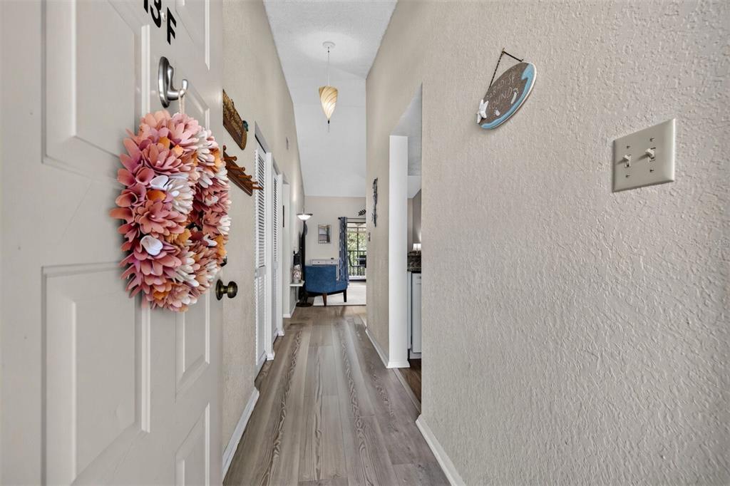 A hallway with light wood-look flooring leads toward a living area with a blue chair — 11511 113TH STREET UNIT 13F, SEMINOLE, FL