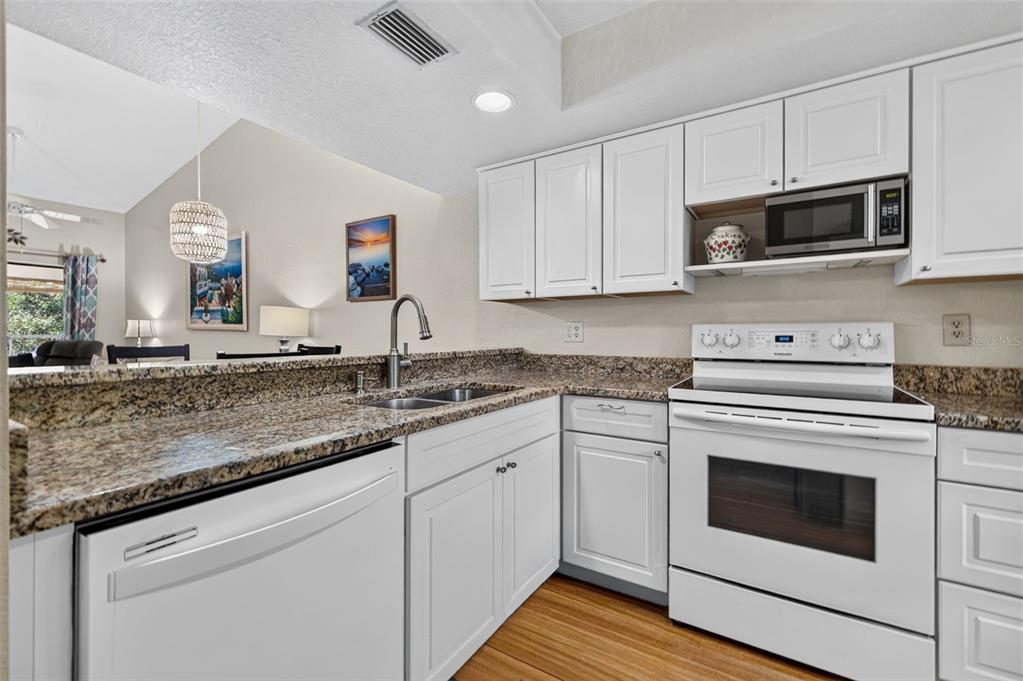 A kitchen with white cabinets, granite countertops, and white appliances, opening to a living area — 11511 113TH STREET UNIT 13F, SEMINOLE, FL