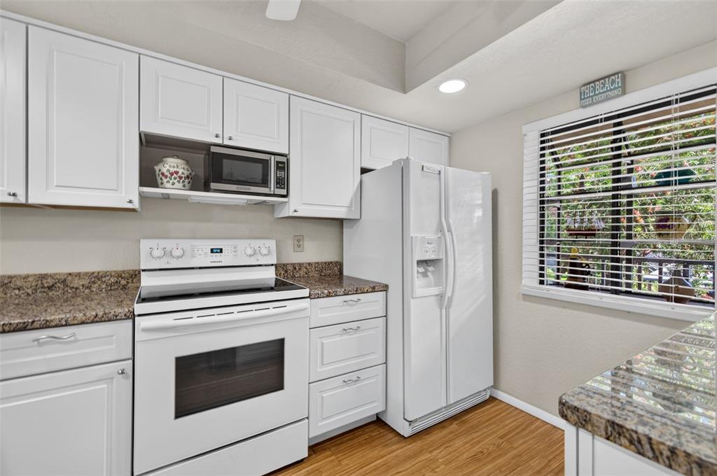 A kitchen features white cabinetry, granite countertops, a white stove, and a white refrigerator — 11511 113TH STREET UNIT 13F, SEMINOLE, FL