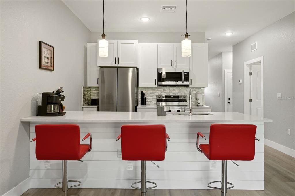 A kitchen features white cabinets, stainless steel appliances, a quartz island, and three red stools — 9409 AGATE STREET, PORT CHARLOTTE, FL