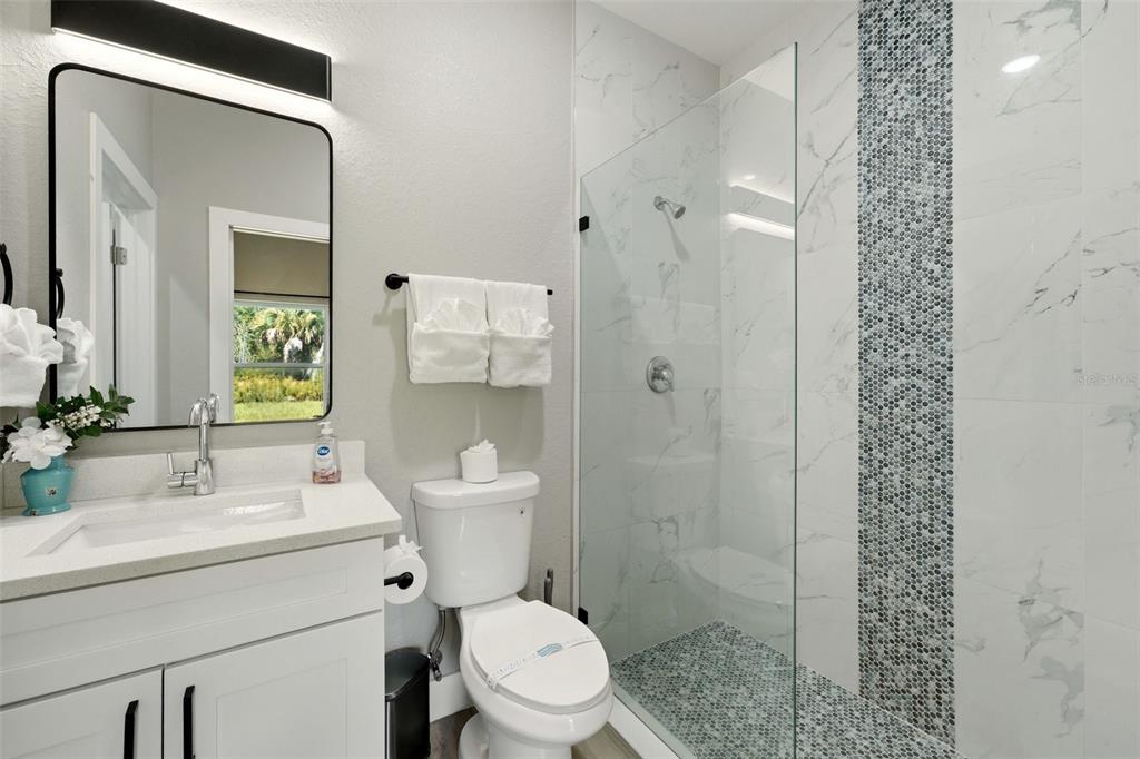 A modern bathroom features a white vanity, a glass-enclosed shower, and a toilet — 9409 AGATE STREET, PORT CHARLOTTE, FL