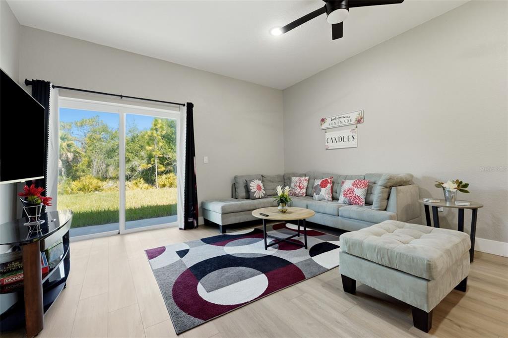 A living room features a gray sectional sofa, a patterned rug, and sliding glass patio doors — 9409 AGATE STREET, PORT CHARLOTTE, FL