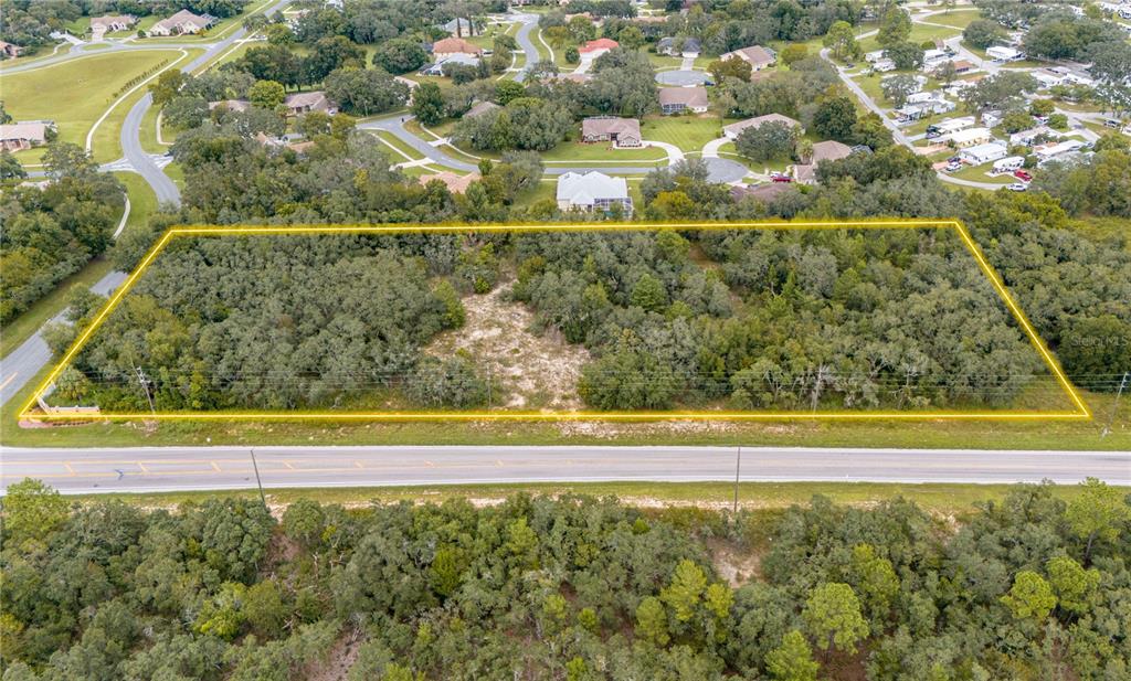 An aerial view shows a rectangular, wooded vacant lot outlined in yellow along a road — COUNTY LINE ROAD, SPRING HILL, FL