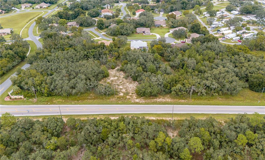 An aerial view shows a vacant, wooded lot situated along a paved road — COUNTY LINE ROAD, SPRING HILL, FL