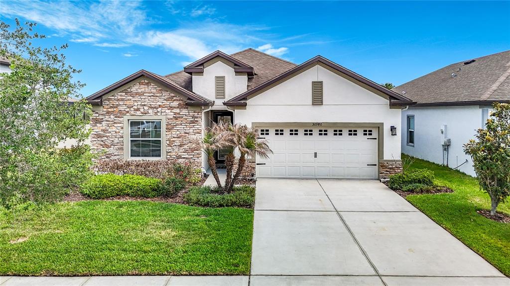 A single-story house features a stone facade, white stucco, and a two-car garage — 30980 JAZZ LEAF PLACE, SAN ANTONIO, FL