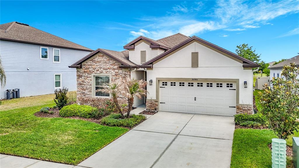 A single-story house features a stone facade, a two-car garage, and a concrete driveway — 30980 JAZZ LEAF PLACE, SAN ANTONIO, FL