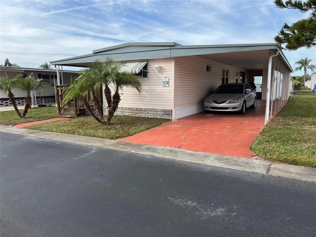A light-colored mobile home features a carport, a red concrete driveway, and small palm trees — 11300 124TH AVENUE UNIT 165, LARGO, FL
