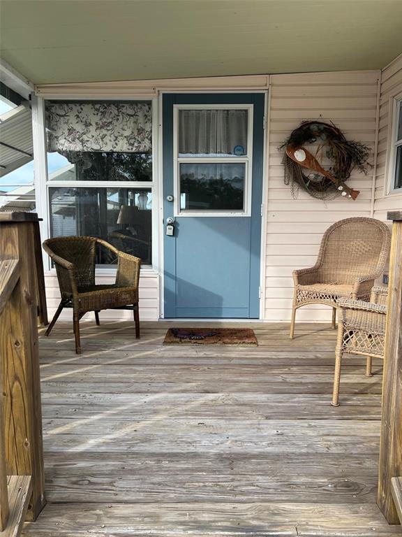 A wooden porch features three wicker chairs, a blue door, and a decorative wall wreath — 11300 124TH AVENUE UNIT 165, LARGO, FL