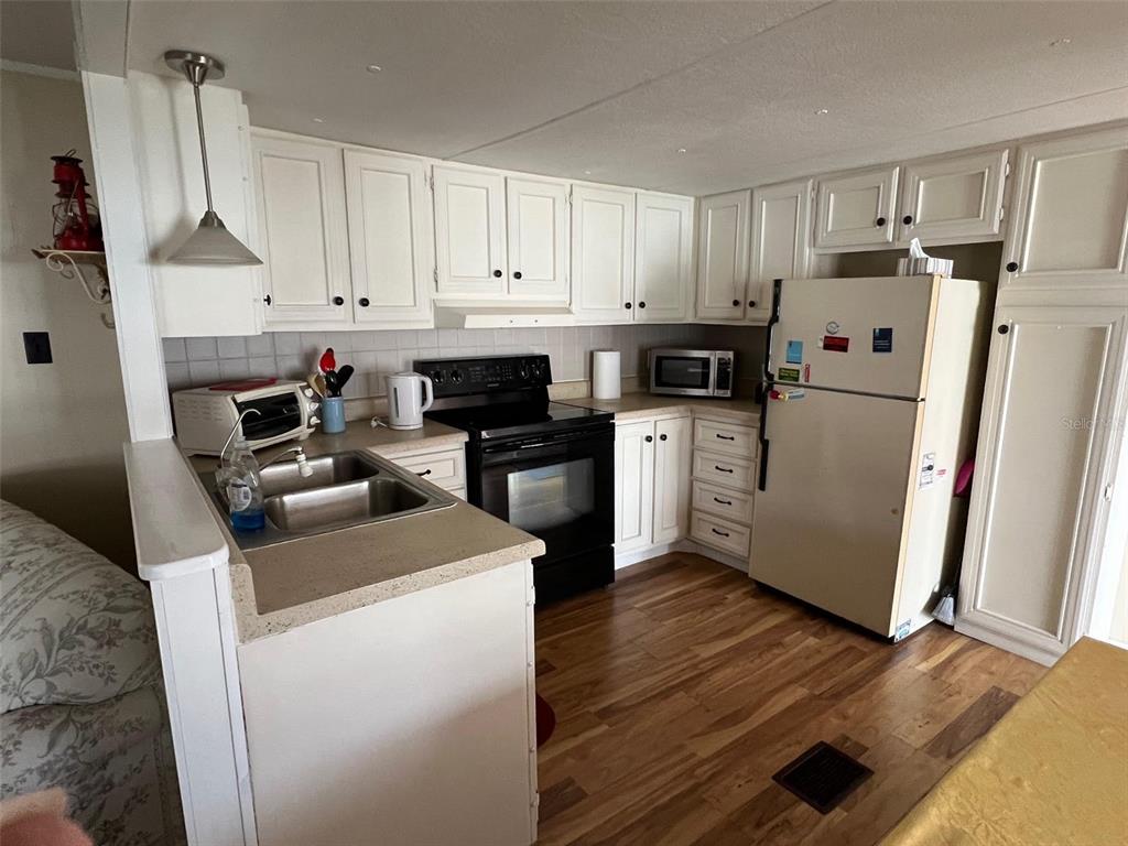 A kitchen features white cabinets, black appliances, a double sink, and wood-look flooring — 11300 124TH AVENUE UNIT 165, LARGO, FL