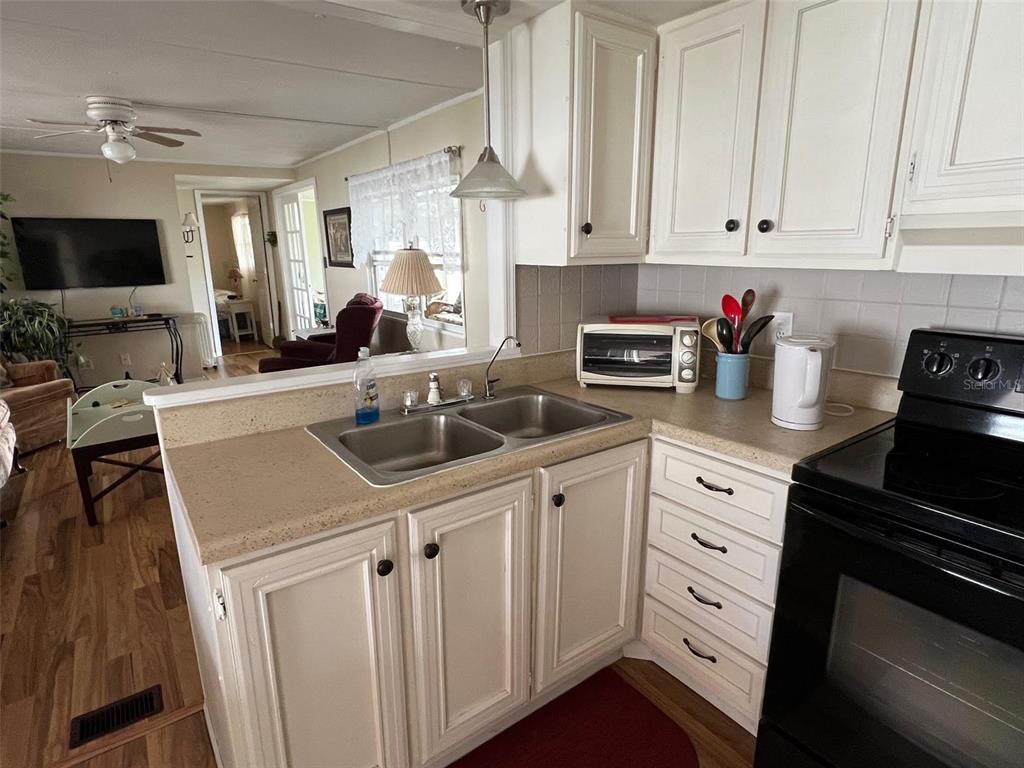 A kitchen with white cabinets, a double sink, and a black stove overlooks a living area — 11300 124TH AVENUE UNIT 165, LARGO, FL