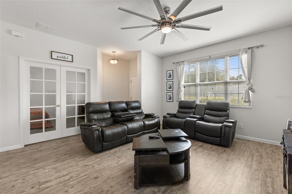 A living room features dark leather reclining furniture, a wooden coffee table, and wood-look flooring — 2427 LINER AVENUE, APOPKA, FL