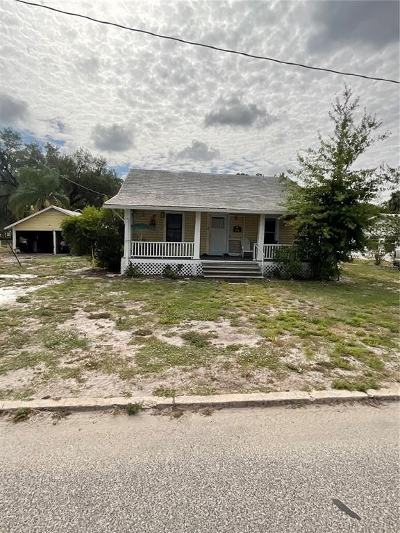 A yellow house with a front porch and a detached garage sits on a sandy lot — 628 E MAGNOLIA STREET, ARCADIA, FL
