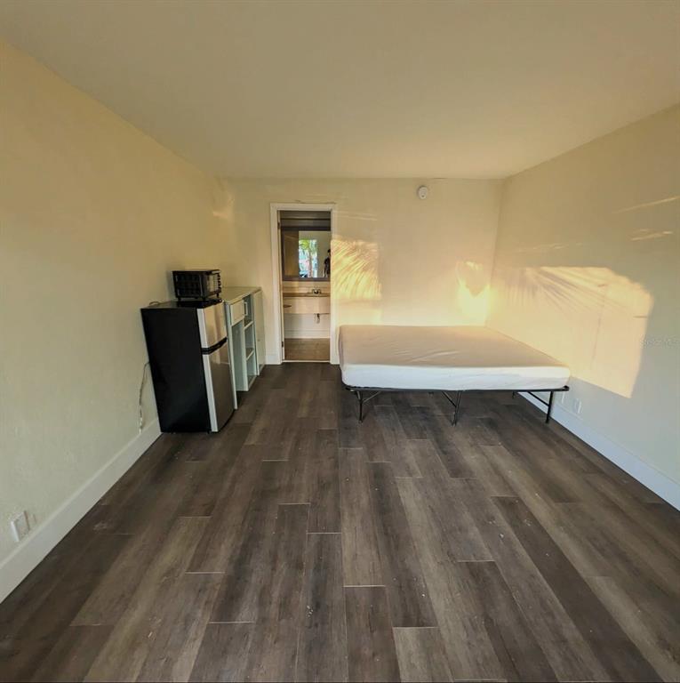 A studio room features wood-look flooring, a bed frame, a small refrigerator, and a bathroom — 7150 N TAMIAMI TRL UNIT S503, SARASOTA, FL