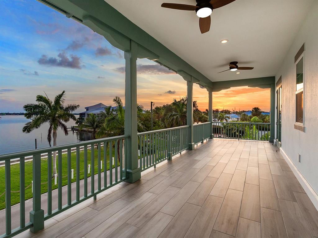 A covered balcony with wood-look tile flooring, green railings, and ceiling fans overlooks a waterfront view — 4024 11TH STREET COURT W, PALMETTO, FL