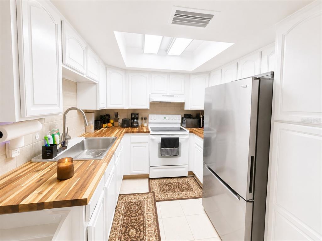 A kitchen features white cabinets, butcher block countertops, a stainless steel refrigerator, and a skylight — 35 ALMOND ROAD, OCALA, FL