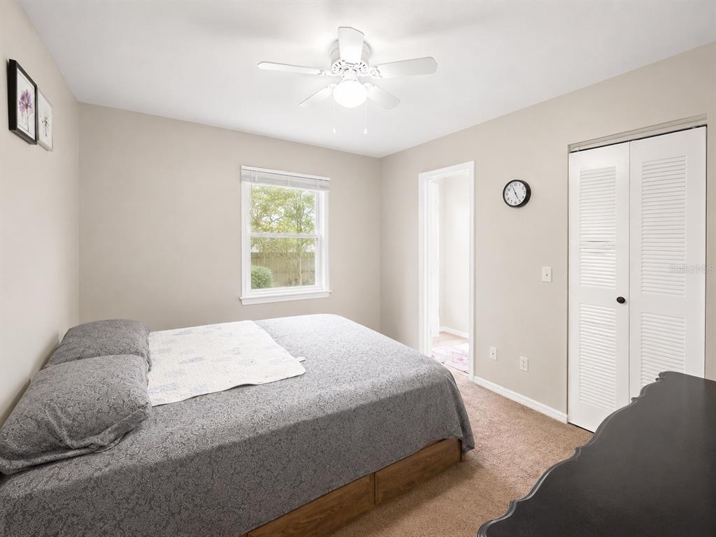A bedroom features a bed with a gray patterned comforter, a ceiling fan, and carpet — 35 ALMOND ROAD, OCALA, FL