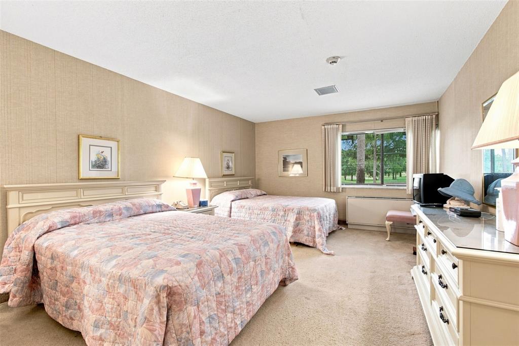 A bedroom features two beds with floral quilts, beige wallpaper, and a white dresser — 36750 US HIGHWAY 19 UNIT 21105, PALM HARBOR, FL