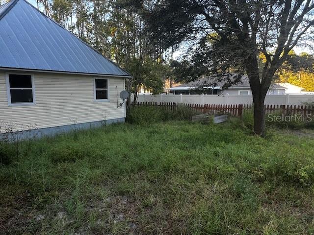 The exterior of a light-colored house with a metal roof sits beside an overgrown yard — 33 SEVEN WONDERS TRAIL, PALM COAST, FL