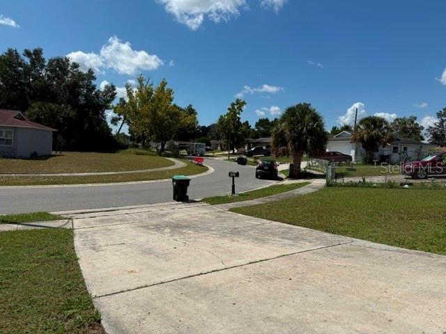 A concrete driveway leads to a suburban street with houses, trees, and a trash bin — 4521 SAN SEBASTIAN CIRCLE, ORLANDO, FL
