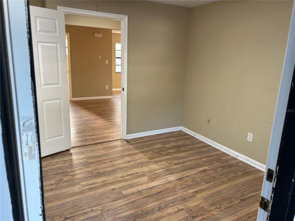 An empty room with wood-look flooring and tan walls leads into an adjacent room — 2945 NE 3RD STREET UNIT 203, OCALA, FL
