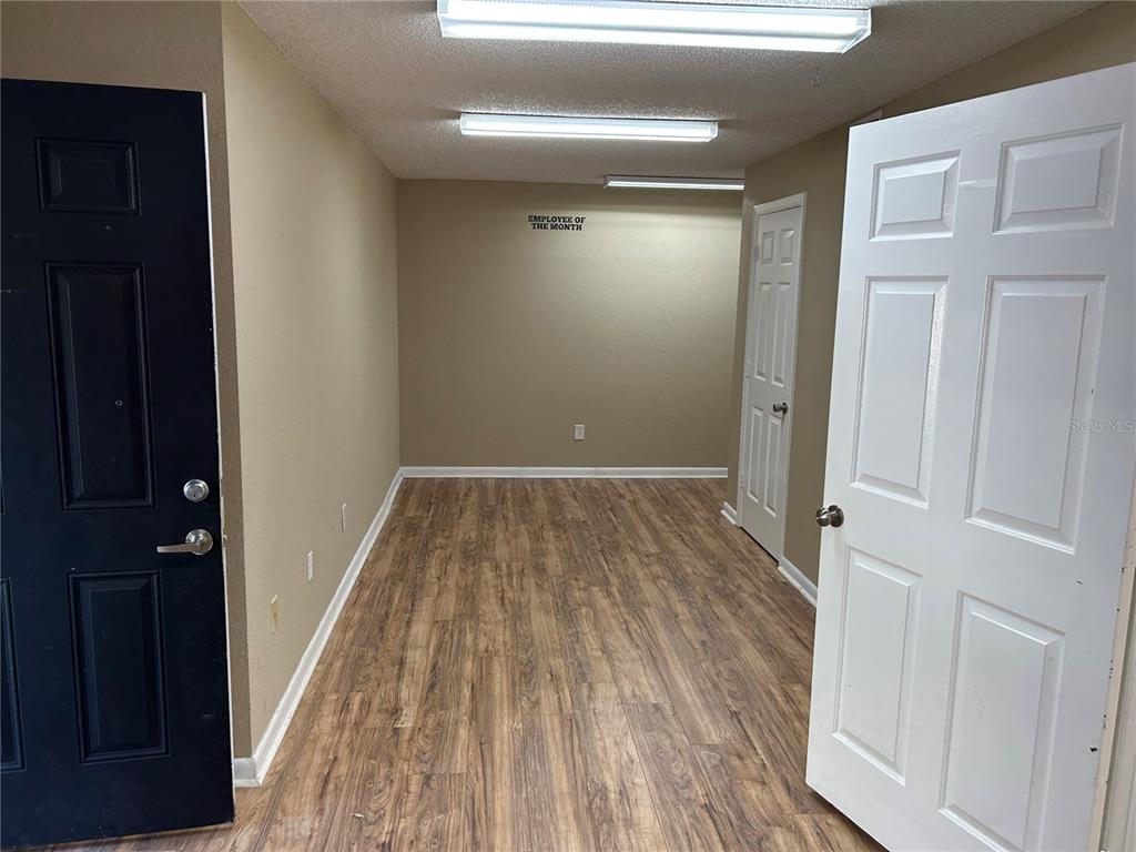 An empty office room features wood-look flooring, beige walls, and two overhead fluorescent light fixtures — 2945 NE 3RD STREET UNIT 203, OCALA, FL