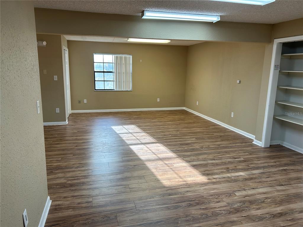 An empty room features wood-look laminate flooring, beige walls, a window, and built-in shelving — 2945 NE 3RD STREET UNIT 203, OCALA, FL