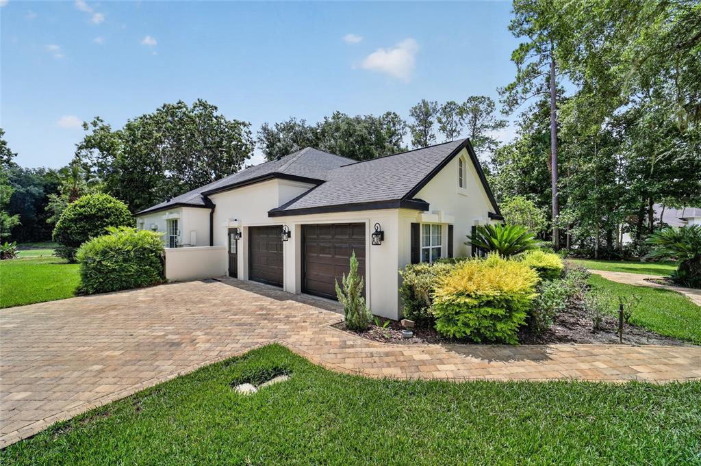 The exterior of a house features a paved driveway, two garage doors, and landscaped gardens — 7050 SE 12TH CIRCLE, OCALA, FL