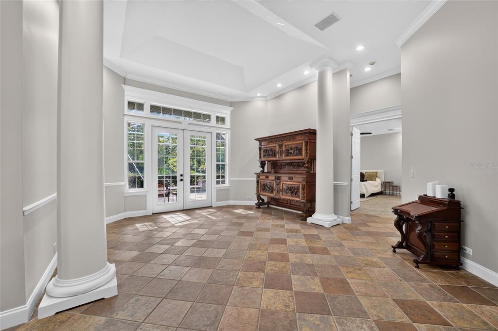 A spacious room with tile flooring, two large columns, and double glass doors to outside — 7050 SE 12TH CIRCLE, OCALA, FL