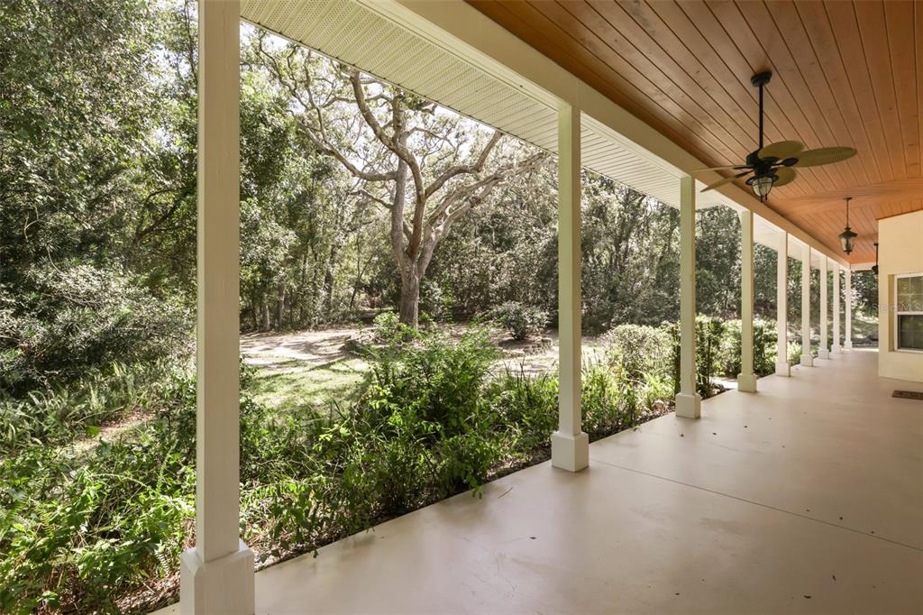 A covered porch with a wood-paneled ceiling overlooks a wooded backyard with mature trees — 1685 MANOR WAY, DELAND, FL