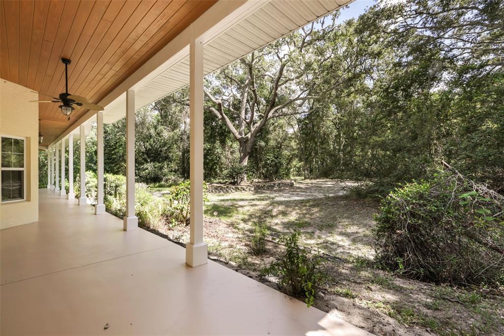 A covered porch with a wood-paneled ceiling overlooks a sandy yard with mature trees — 1685 MANOR WAY, DELAND, FL