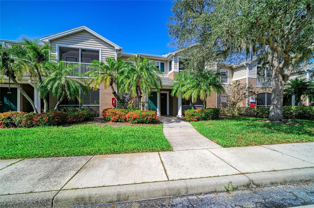 A two-story apartment building with a concrete walkway, palm trees, and landscaped flower beds — 8932 MANOR LOOP UNIT 102, BRADENTON, FL