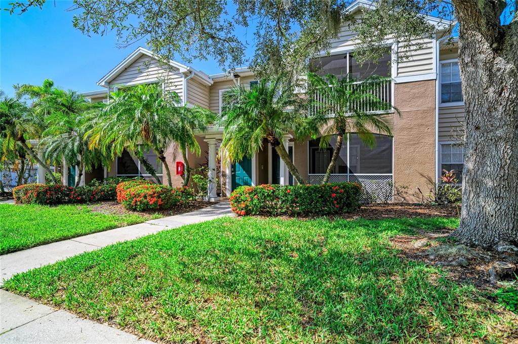 A two-story tan townhouse with a screened balcony and a landscaped front yard — 8932 MANOR LOOP UNIT 102, BRADENTON, FL