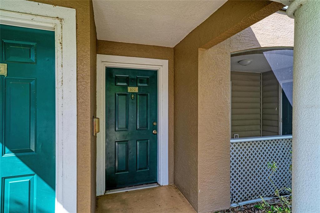 A dark green front door labeled 102 is situated on a covered outdoor entryway — 8932 MANOR LOOP UNIT 102, BRADENTON, FL