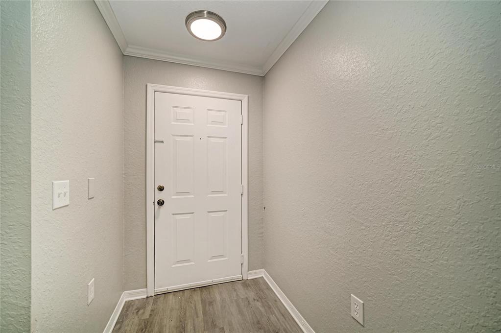 An entryway features a white front door, light gray walls, and wood-look flooring — 8932 MANOR LOOP UNIT 102, BRADENTON, FL