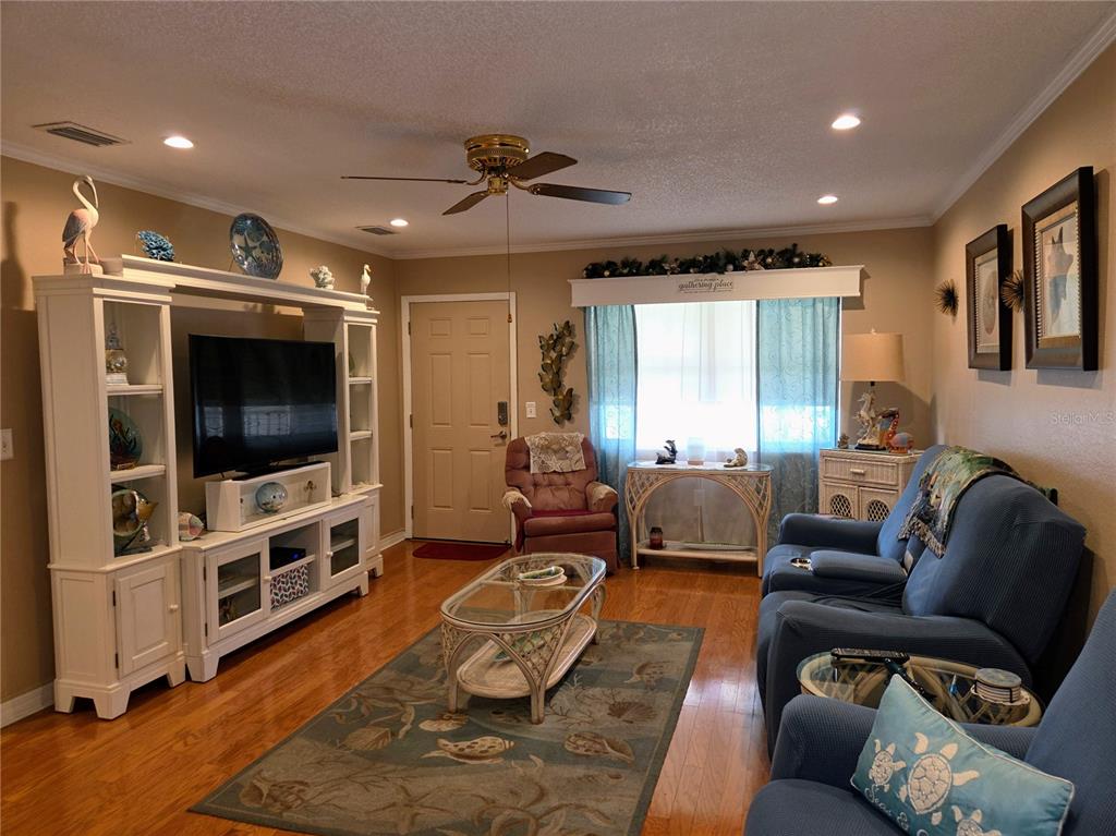 A living room features a white entertainment center, blue sofa, area rug, and hardwood floors — 10036 63RD AVENUE N UNIT 23, ST PETERSBURG, FL
