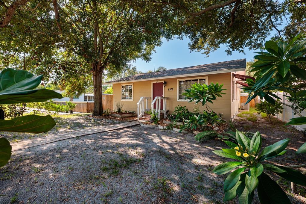 A single-story house with tan siding and a red front door sits under large trees — 6376 4TH AVENUE S, ST PETERSBURG, FL