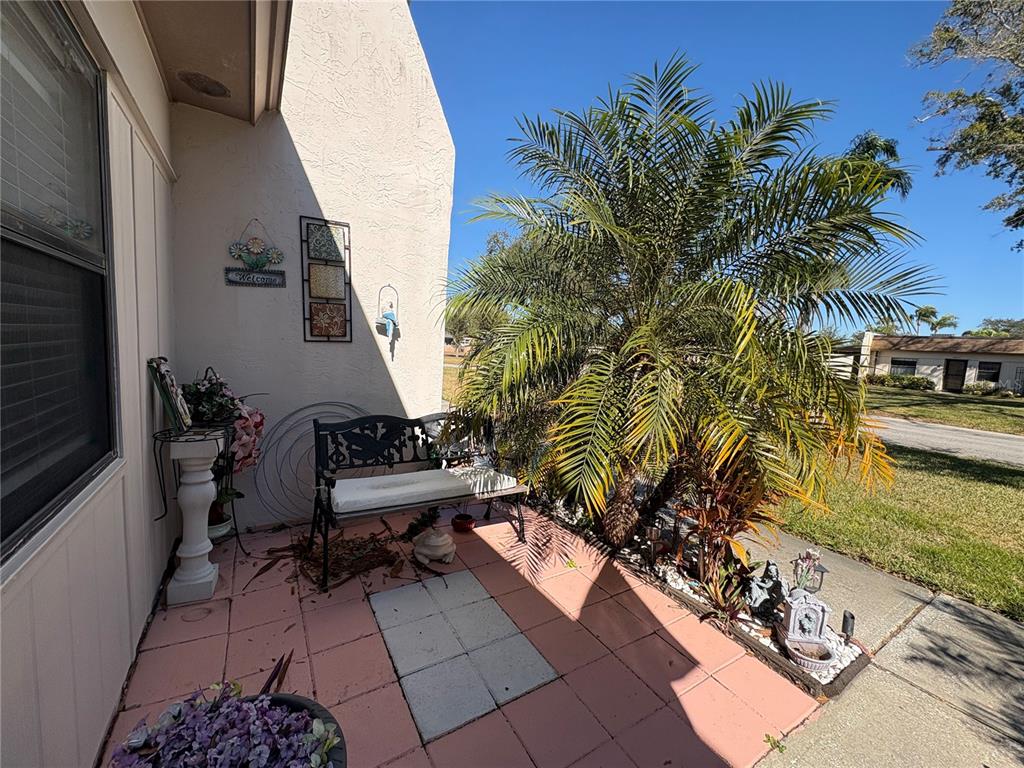 A patio with a metal bench, a palm tree, and decorative items on a tiled floor — 1606 FLINT DRIVE W, CLEARWATER, FL