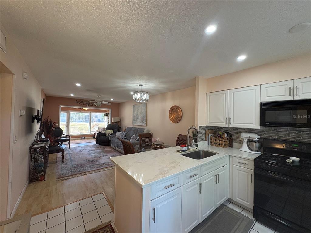 A kitchen with white cabinets and a quartz countertop overlooks an open-concept living area — 1606 FLINT DRIVE W, CLEARWATER, FL