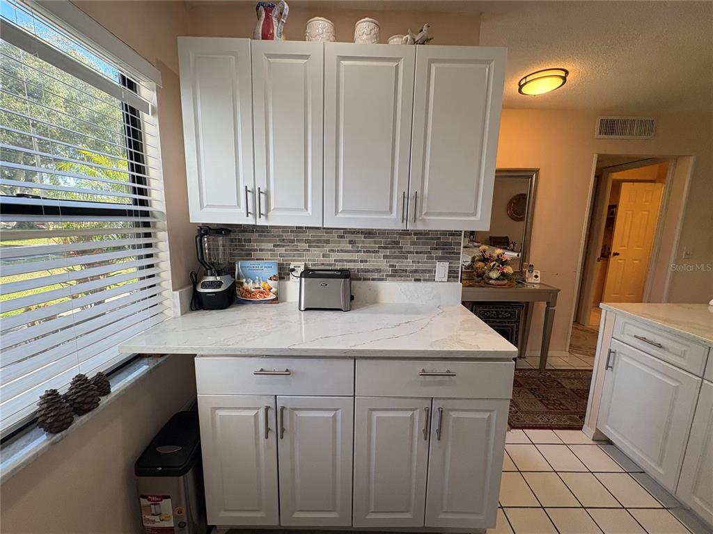 A kitchen area features white cabinets, a marble-look countertop, and a tiled backsplash — 1606 FLINT DRIVE W, CLEARWATER, FL