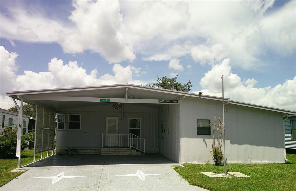 A single-story manufactured home with a large carport and a concrete driveway featuring star designs — 34145 BROWN BAYOU, WESLEY CHAPEL, FL