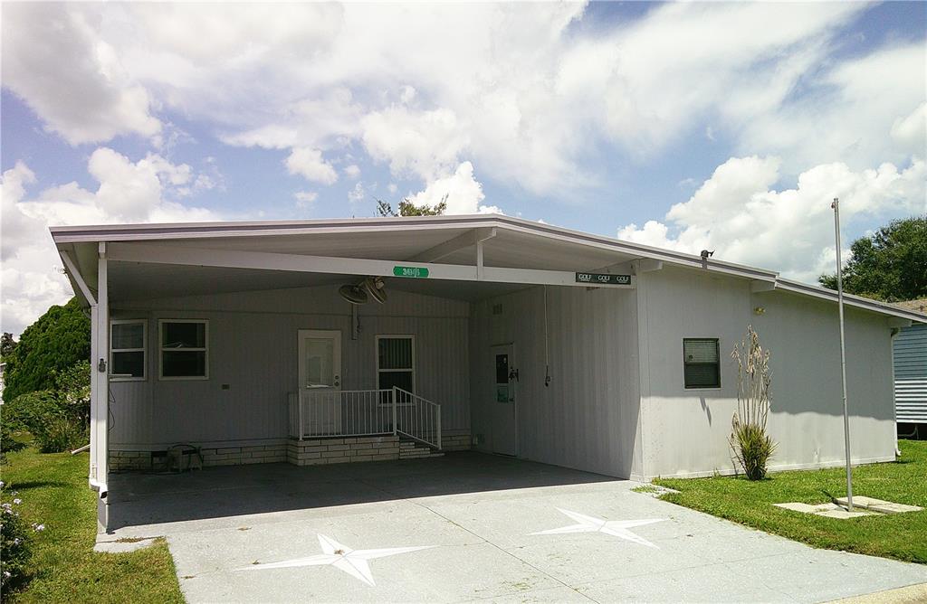 A single-story house with a large carport, concrete driveway, and white siding under a cloudy sky — 34145 BROWN BAYOU, WESLEY CHAPEL, FL