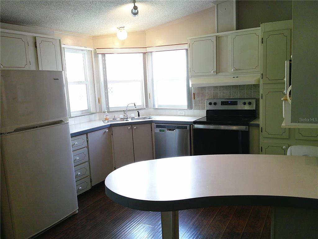 A kitchen features white cabinets, a white refrigerator, a dishwasher, and a curved breakfast bar — 34145 BROWN BAYOU, WESLEY CHAPEL, FL