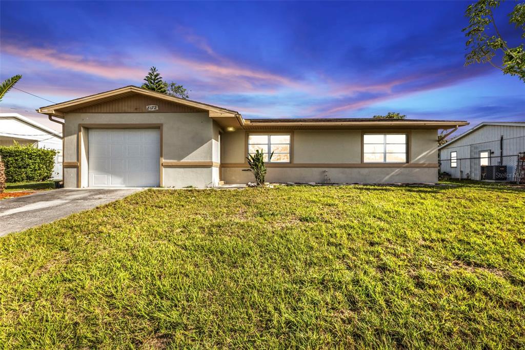 A single-story house with a garage, beige stucco exterior, and a grassy front yard — 8172 TRIONFO AVENUE, NORTH PORT, FL